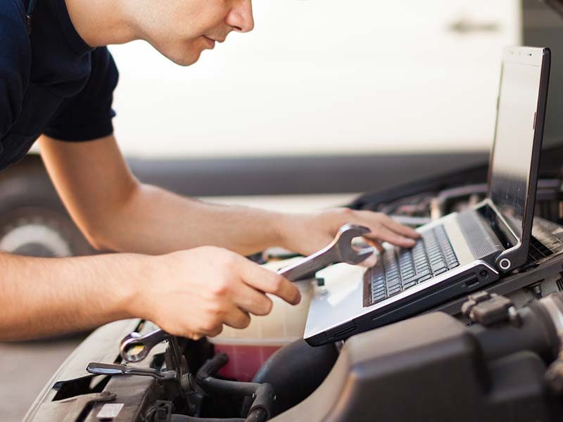 Mechanic using laptop on top of car engine bay